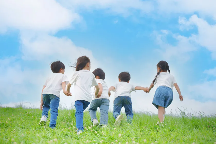 青空と芝生の中で子供たちが走っている写真